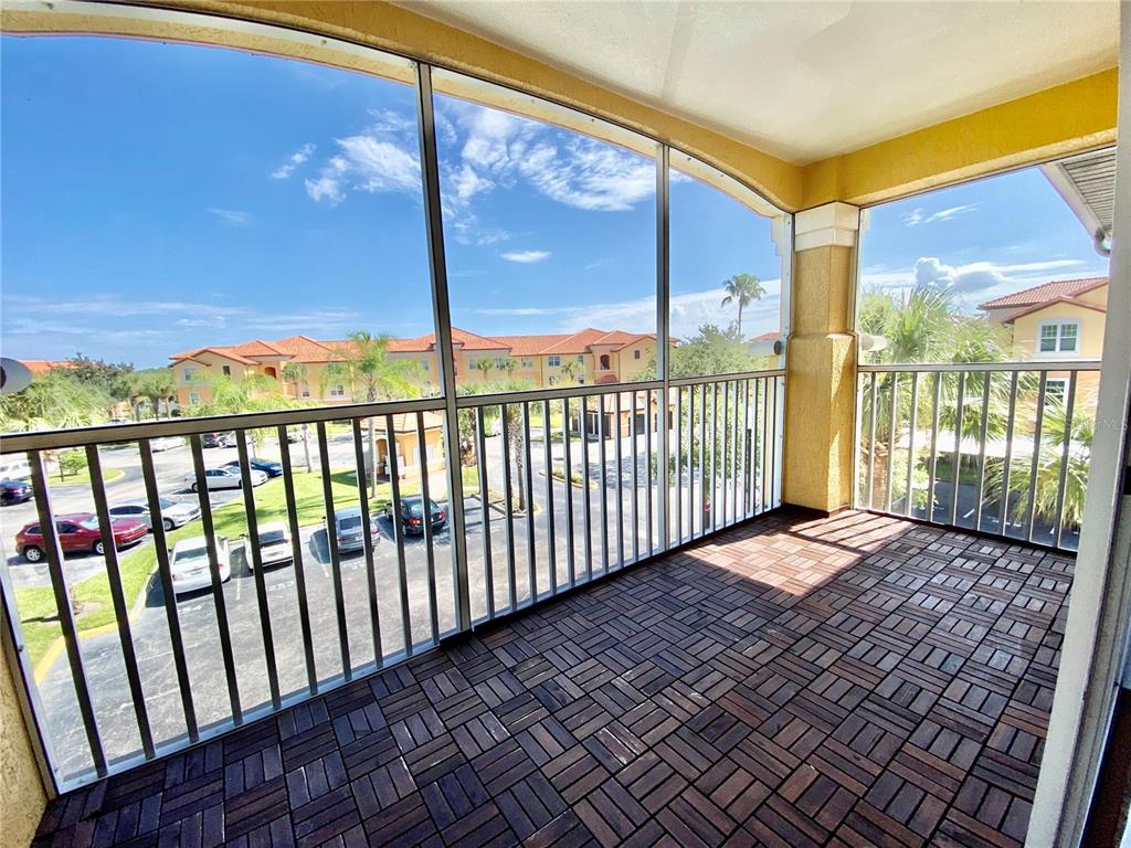A screened-in balcony features dark wood-look floor tiles and a view of a parking lot — 5467 VINELAND ROAD UNIT 6301, ORLANDO, FL