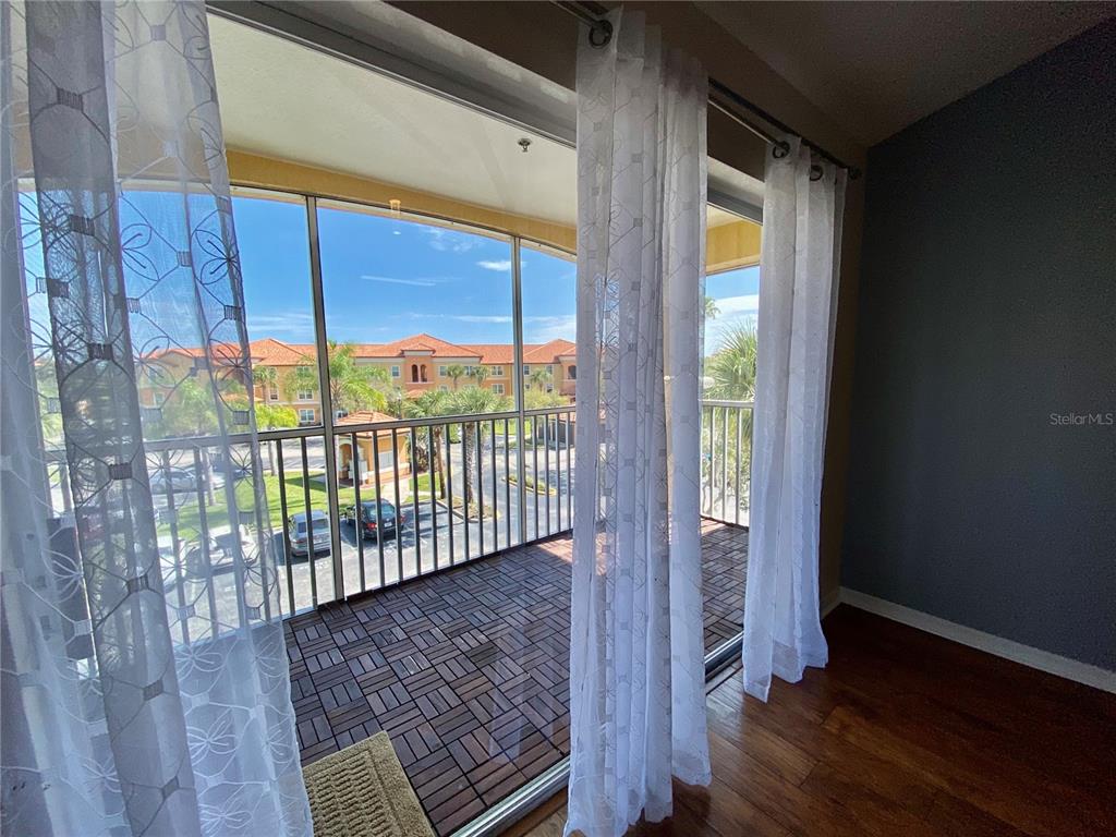 A balcony with tiled flooring and a screen enclosure overlooks a parking lot and buildings — 5467 VINELAND ROAD UNIT 6301, ORLANDO, FL