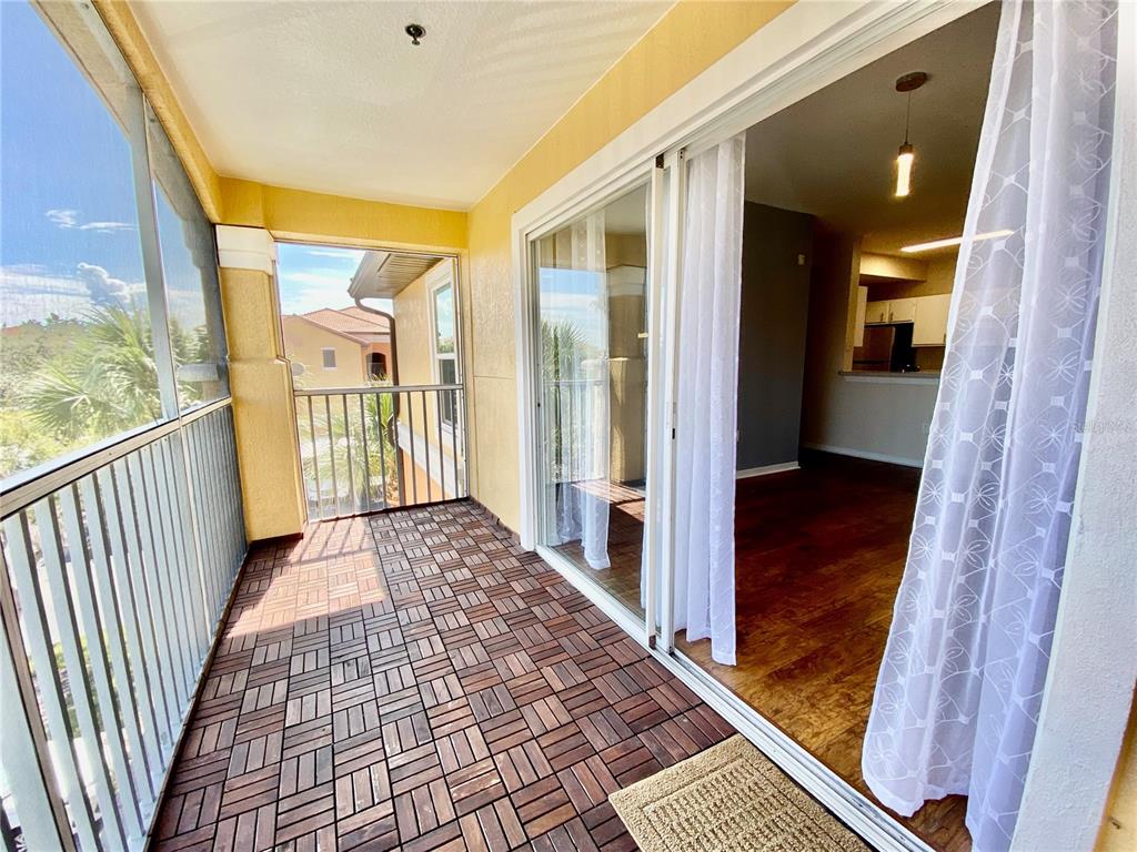 A screened-in balcony features interlocking wood deck tiles and sliding glass doors to an interior — 5467 VINELAND ROAD UNIT 6301, ORLANDO, FL