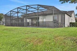 A rear view of a house with a screened-in patio and a grassy backyard — 163 KENNY BOULEVARD, HAINES CITY, FL