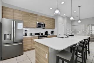 A modern kitchen features light wood cabinets, stainless steel appliances, and a large white island — 163 KENNY BOULEVARD, HAINES CITY, FL