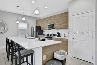 A modern kitchen features a white island with bar stools, wood cabinetry, and stainless steel appliances — 163 KENNY BOULEVARD, HAINES CITY, FL