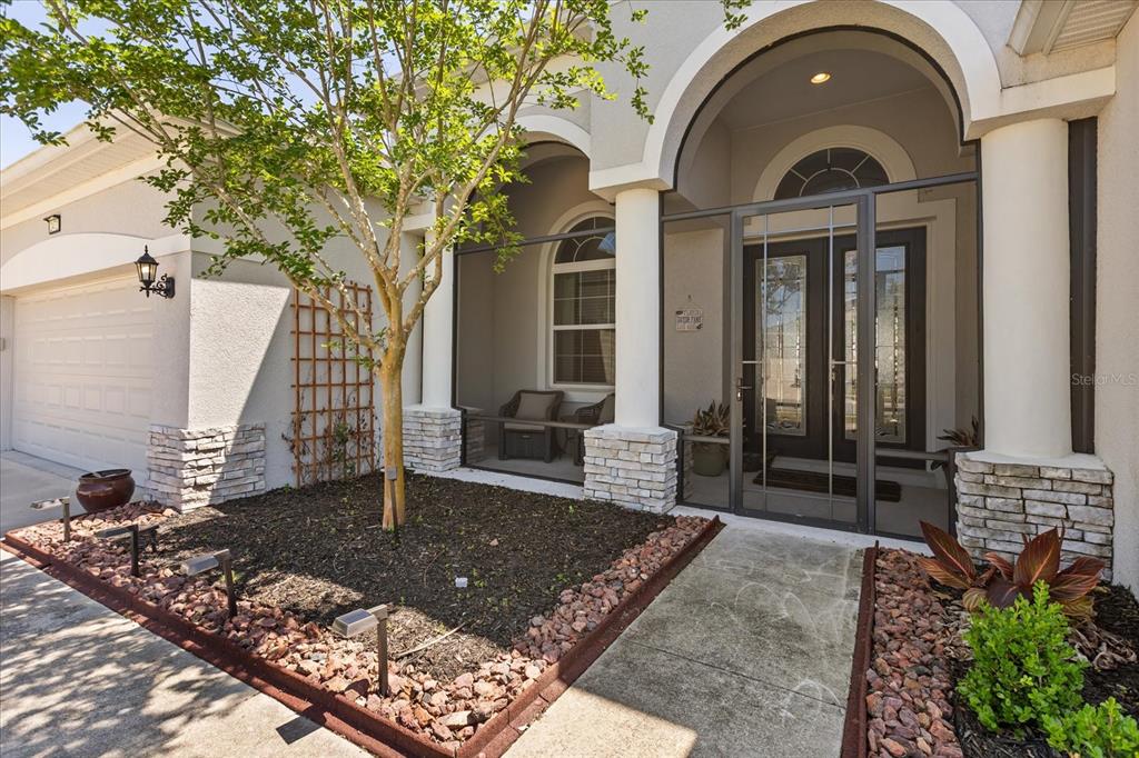 A front exterior view shows a screened entryway, a small garden bed, and a garage — 2472 PAWTUCKET PASS, MOUNT DORA, FL