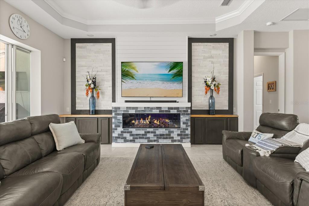 A living room features a fireplace with a tiled surround, a wall-mounted television, and sofas — 2472 PAWTUCKET PASS, MOUNT DORA, FL