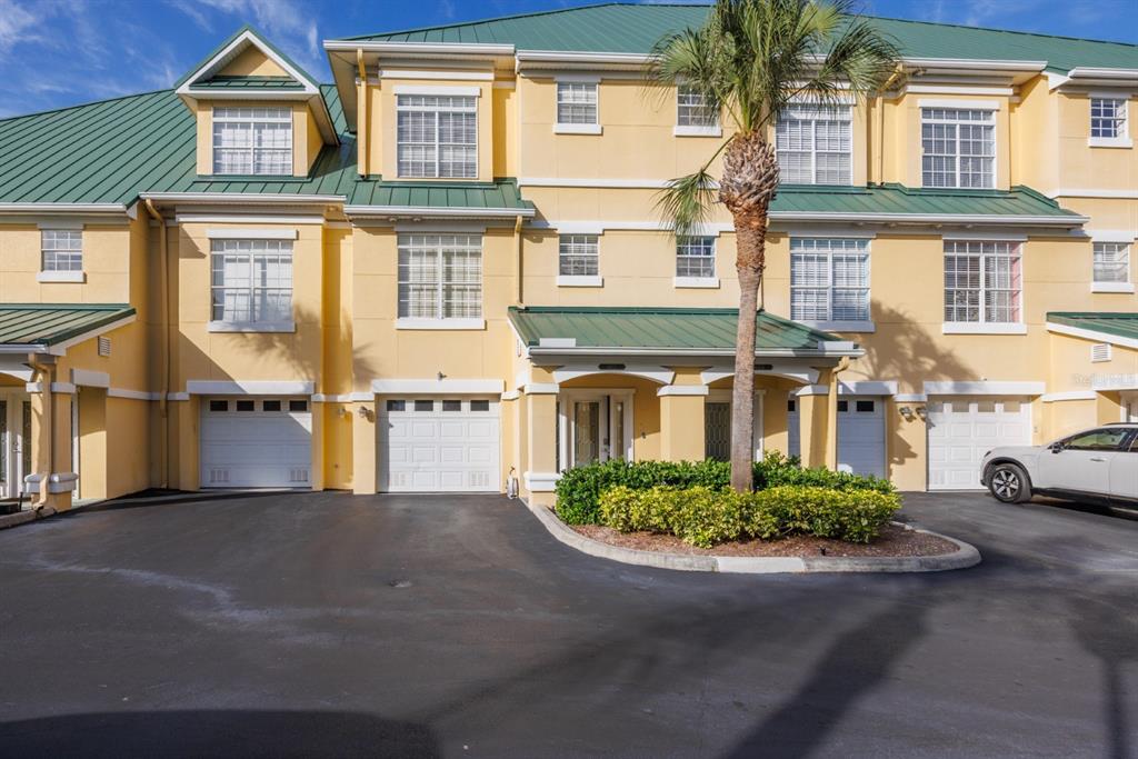 A multi-story yellow townhouse complex with green metal roofs, white garage doors, and a palm tree — 6432 SUNSET BAY CIRCLE, APOLLO BEACH, FL