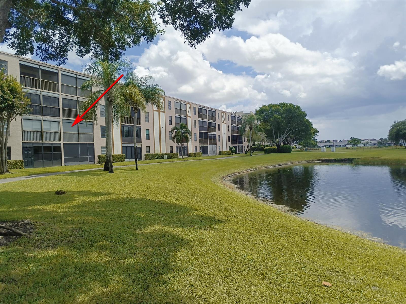 A multi-story apartment building with screened balconies overlooks a pond and grassy lawn — 7280 Amberly Lane # 207, Delray Beach FL 33446, DELRAY BEACH, FL