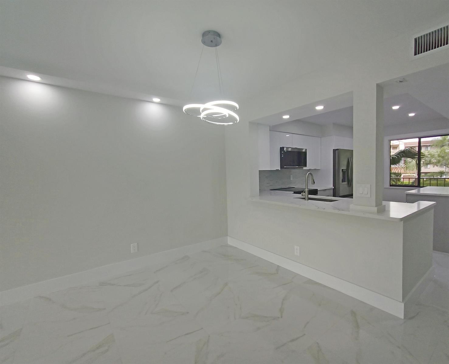 A dining area with a modern chandelier, marble-look tile floors, and a kitchen pass-through window — 7280 Amberly Lane # 207, Delray Beach FL 33446, DELRAY BEACH, FL