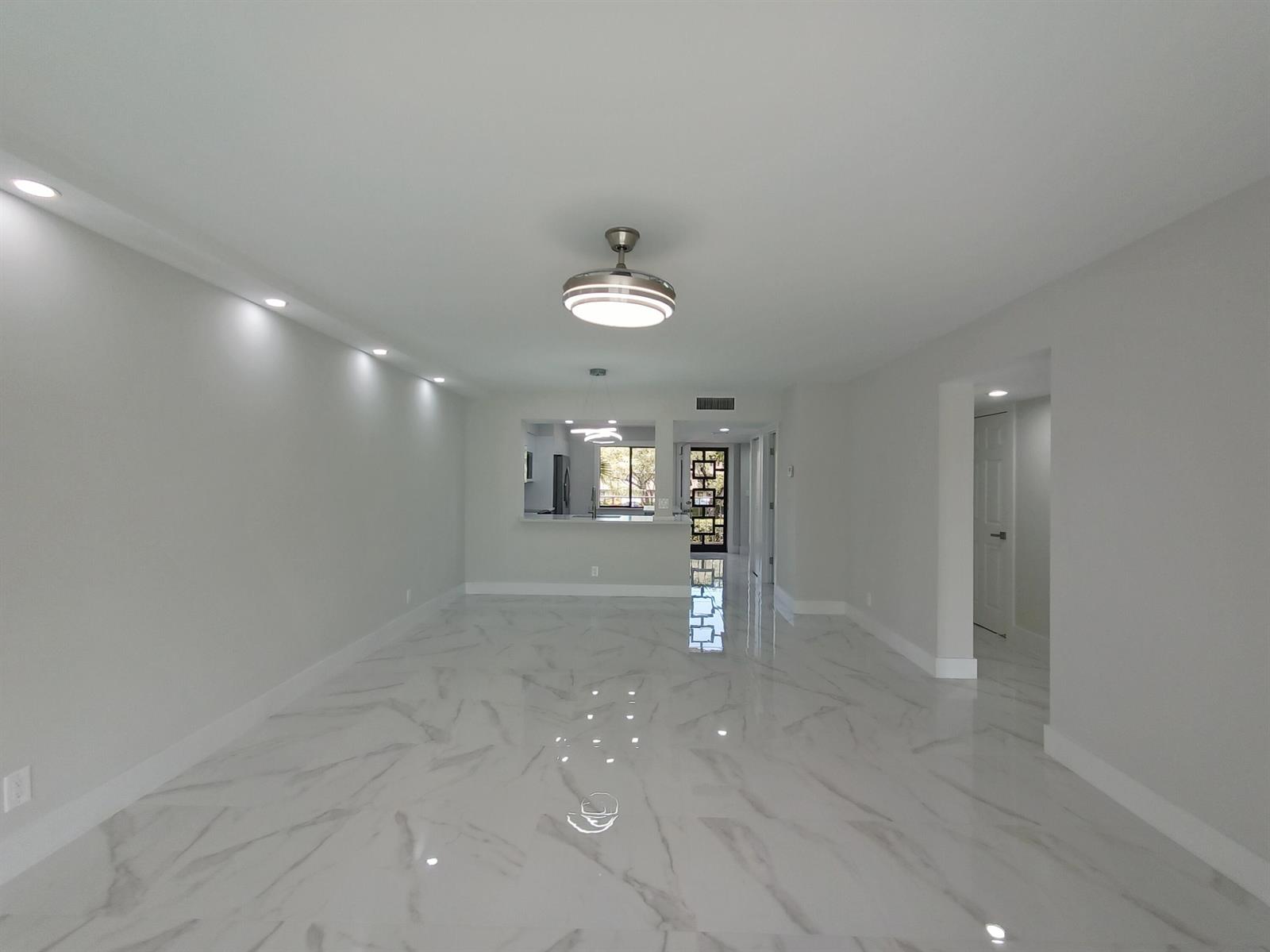 A bright, empty living room features white marble-look tile flooring and recessed ceiling lighting — 7280 Amberly Lane # 207, Delray Beach FL 33446, DELRAY BEACH, FL