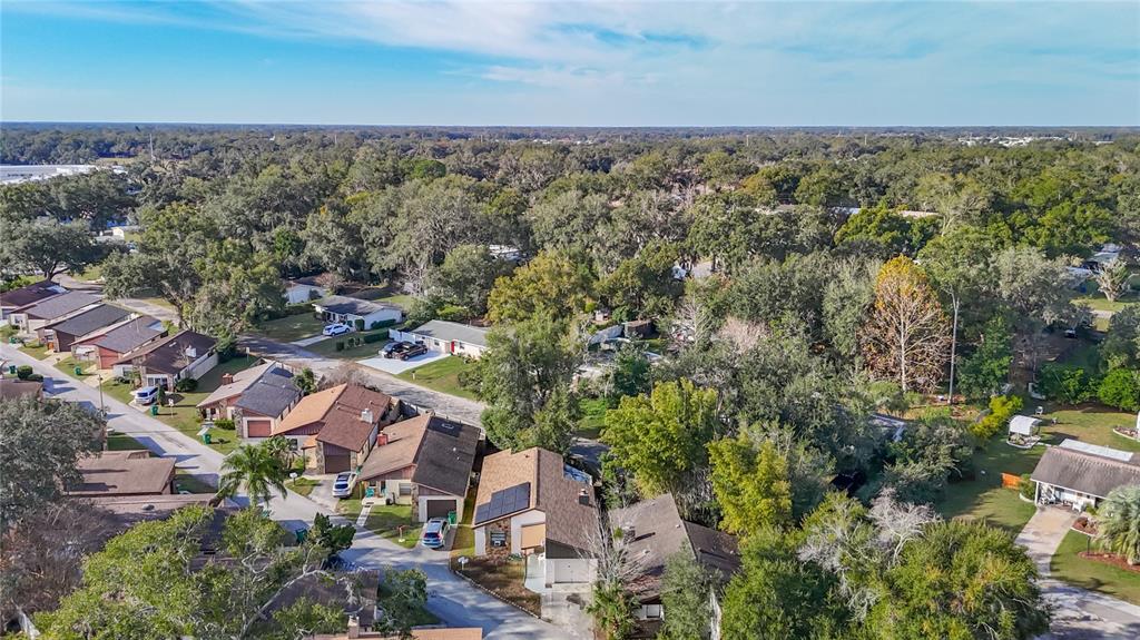 An aerial view shows a suburban neighborhood with several houses, paved streets, and mature trees — 5937 FOREST LANE, ZEPHYRHILLS, FL