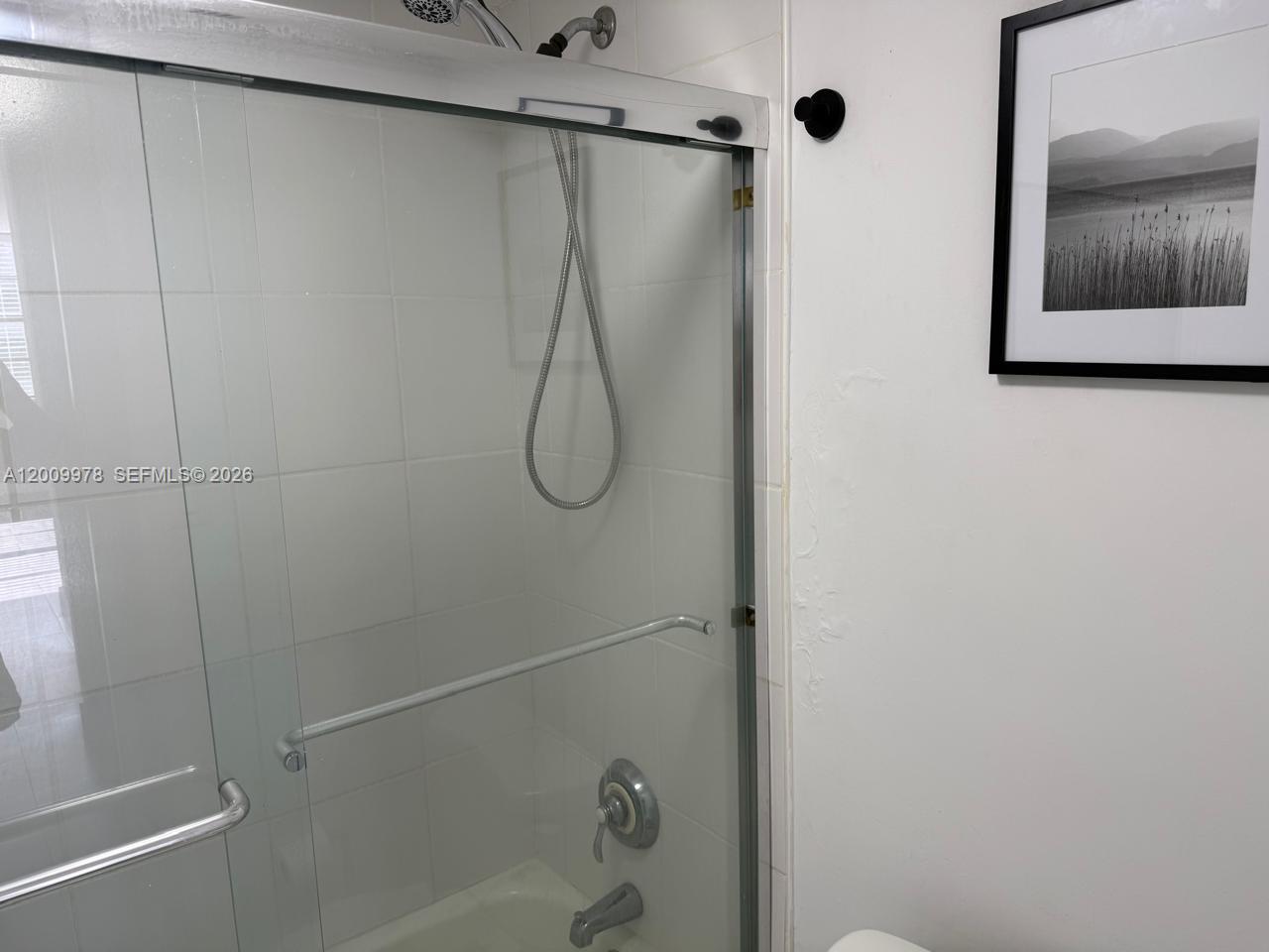 A bathroom features a glass-enclosed shower with white tiled walls and a framed wall art piece — 150 Ocean Lane Dr # 6F, Key Biscayne FL 33149, KEY BISCAYNE, FL