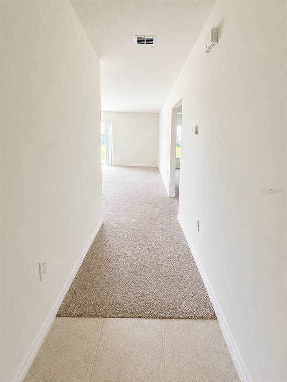 A hallway with tile flooring transitions into a carpeted living area with a sliding glass door — 417 PATRICIA ALFORD DRIVE, HAINES CITY, FL