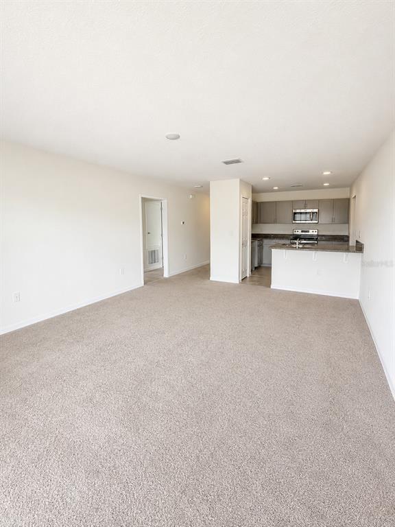 An open-concept living area features beige carpeting and a kitchen with gray cabinets — 417 PATRICIA ALFORD DRIVE, HAINES CITY, FL