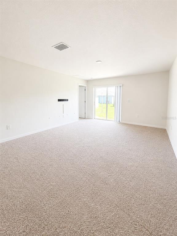 A spacious, carpeted living room features neutral walls, a ceiling vent, and sliding glass doors — 417 PATRICIA ALFORD DRIVE, HAINES CITY, FL