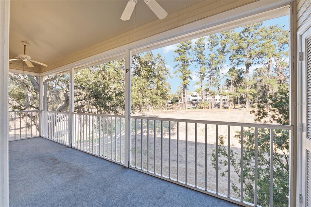 A screened-in porch with gray carpeting, white railings, and a ceiling fan overlooking trees — 3615 NW 104TH DRIVE UNIT 102, GAINESVILLE, FL