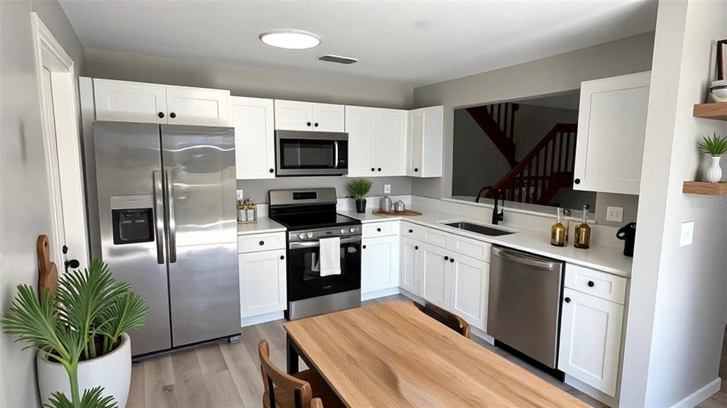 A kitchen features white cabinets, stainless steel appliances, and a wooden dining table — 4578 PHEASANT RUN DRIVE UNIT 7B, ORLANDO, FL