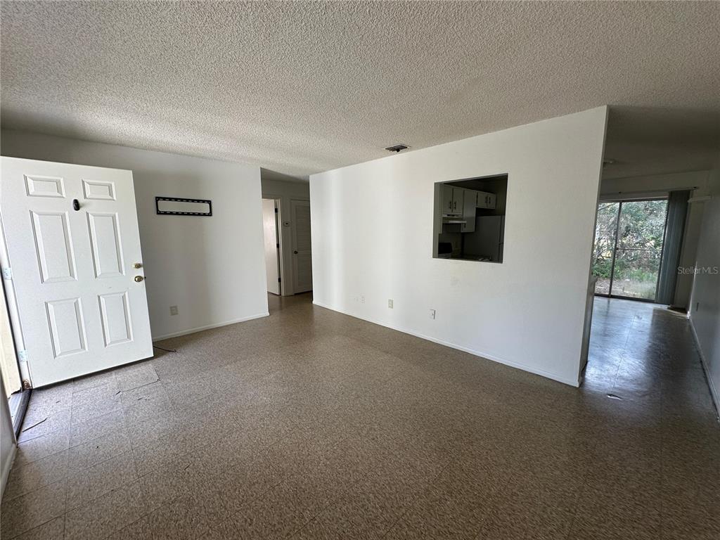 An interior view shows a living room with beige flooring, white walls, and a kitchen pass-through — 430 S HILL AVENUE UNIT 432, DELAND, FL