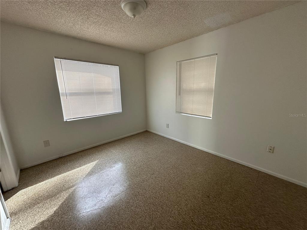 An empty bedroom features beige carpet, white walls, two windows with blinds, and a ceiling light — 430 S HILL AVENUE UNIT 432, DELAND, FL