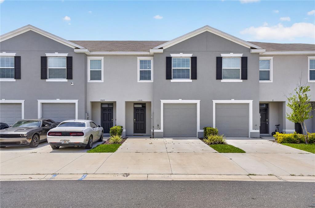 A row of two-story townhomes with gray stucco facades, attached garages, and concrete driveways — 33028 TULIP PETAL LANE, WESLEY CHAPEL, FL