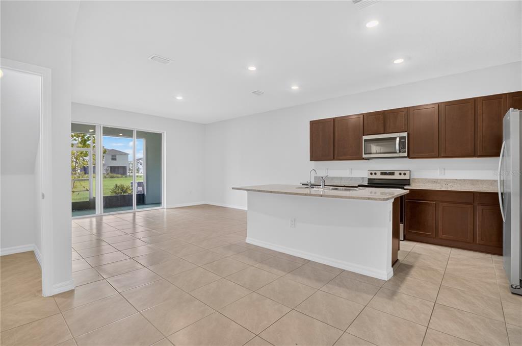 An open-concept kitchen with dark wood cabinets, a granite island, and tile flooring — 33028 TULIP PETAL LANE, WESLEY CHAPEL, FL