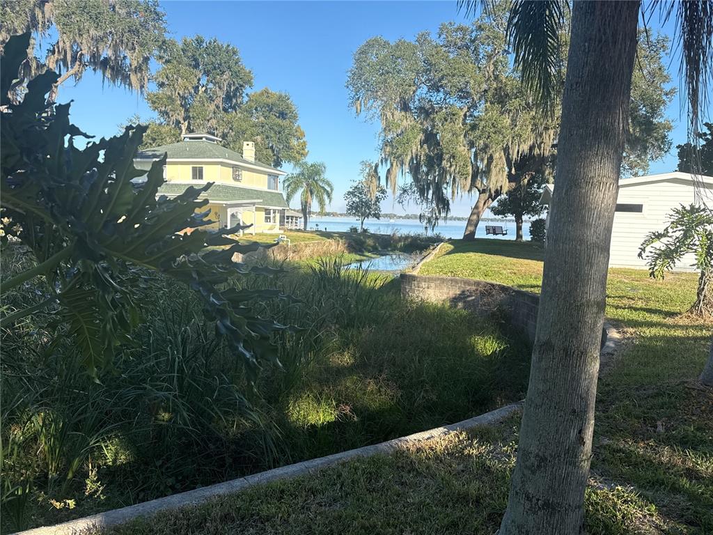 A yellow house sits near a canal leading to a lake with trees and grass — 903 N HARBOR TERRACE, TAVARES, FL