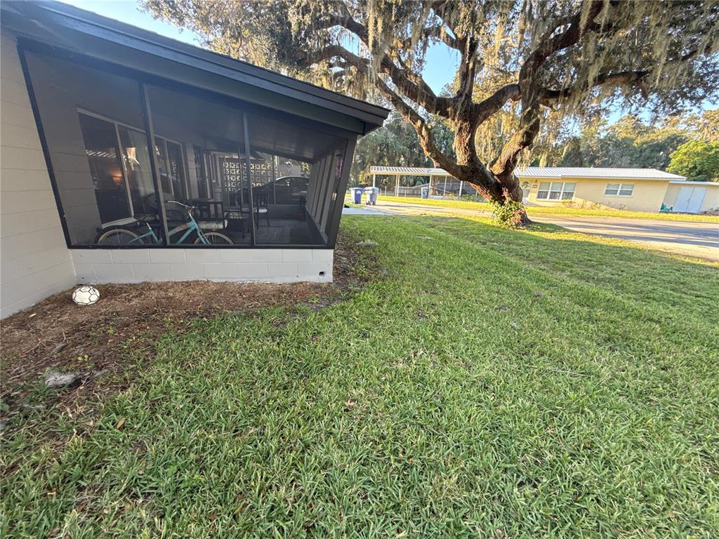 A side view of a house with a screened-in porch and a large oak tree — 903 N HARBOR TERRACE, TAVARES, FL