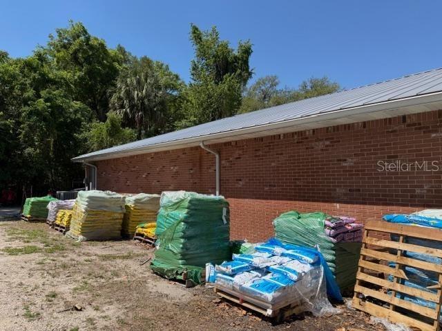 The exterior of a brick building features a metal roof and pallets of bagged materials — 25155 W NEWBERRY ROAD, NEWBERRY, FL