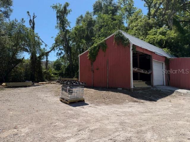A red barn with a metal roof sits on a dirt lot near trees — 25155 W NEWBERRY ROAD, NEWBERRY, FL