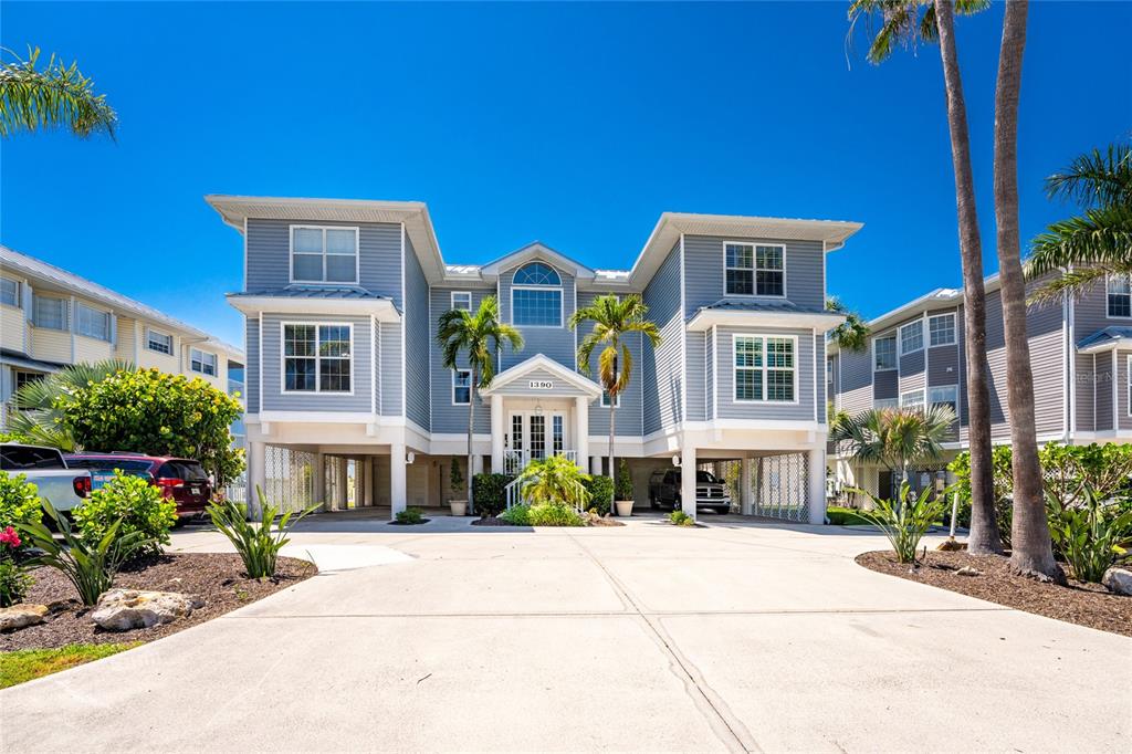 A three-story blue house with elevated living space and a large concrete driveway — 1390 BEACH ROAD UNIT 1, ENGLEWOOD, FL