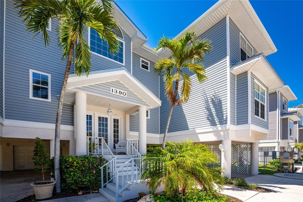A blue-sided two-story house with a raised entrance, palm trees, and a ground-level garage — 1390 BEACH ROAD UNIT 1, ENGLEWOOD, FL