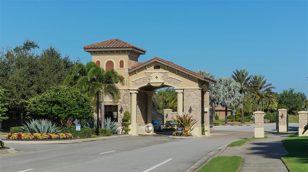 A gated community entrance features a stone archway with a guardhouse and palm trees — 523 GRAND PRESERVE COVE, BRADENTON, FL