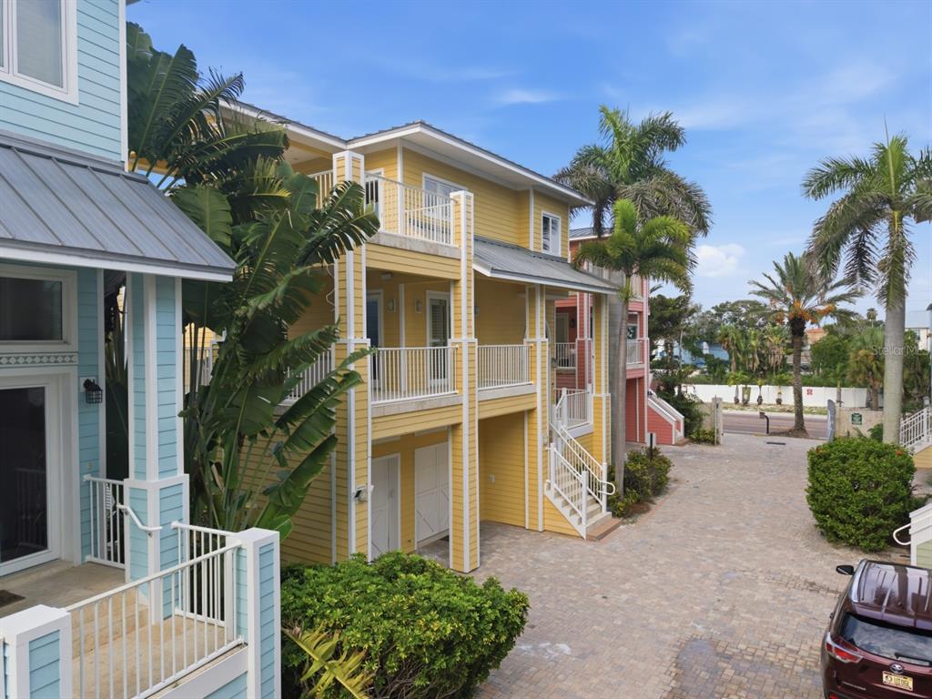 An exterior view of a yellow multi-story coastal house with balconies and a paved driveway — 2718 GULF BOULEVARD UNIT 2, INDIAN ROCKS BEACH, FL