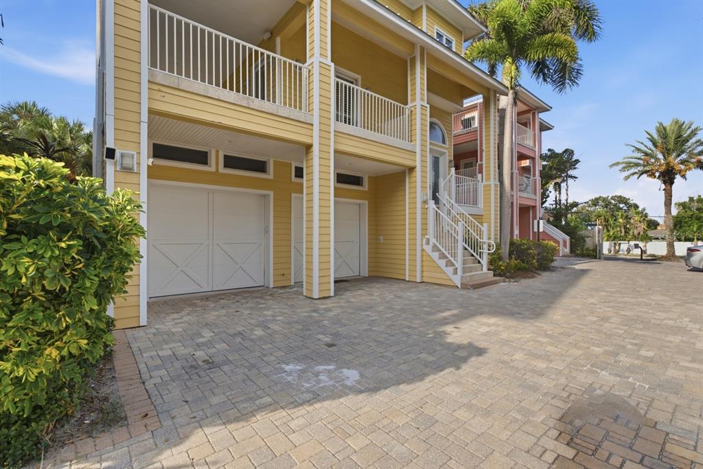 A yellow three-story house with a paved driveway, garage doors, and an exterior staircase — 2718 GULF BOULEVARD UNIT 2, INDIAN ROCKS BEACH, FL