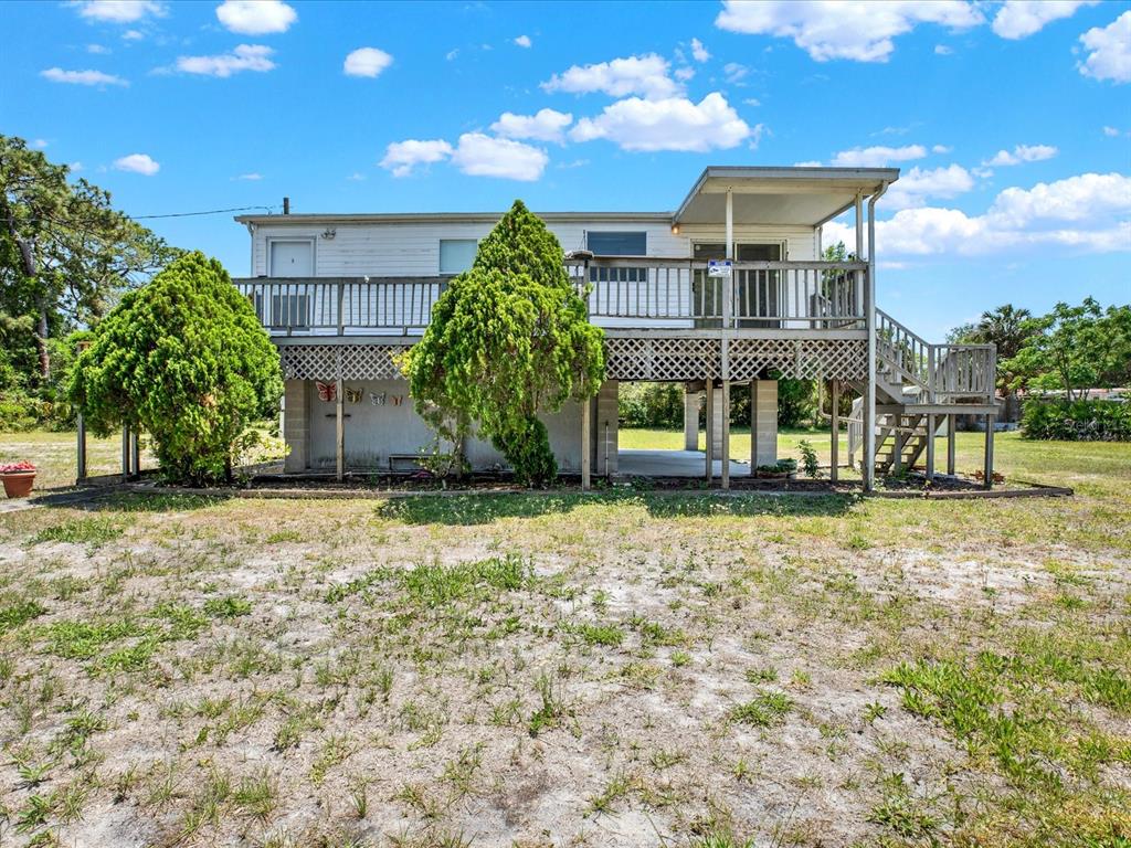 A two-story house with a large wooden deck and lattice skirting stands on a grassy lot — 7606 DETROIT AVENUE, HUDSON, FL