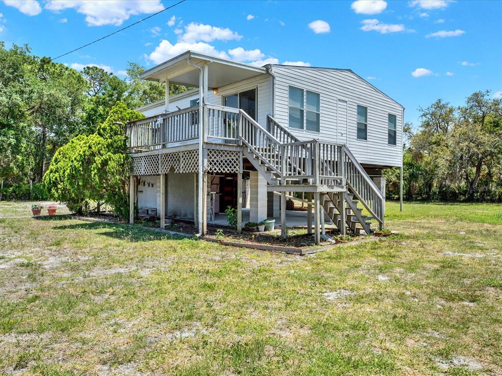 An elevated house with a wooden deck and staircase sits on a grassy lot — 7606 DETROIT AVENUE, HUDSON, FL