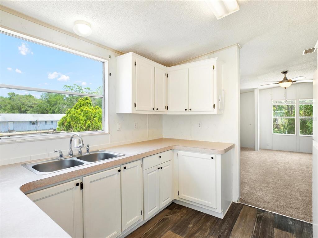 A kitchen with white cabinets, laminate countertops, and a double sink overlooks an outdoor view — 7606 DETROIT AVENUE, HUDSON, FL