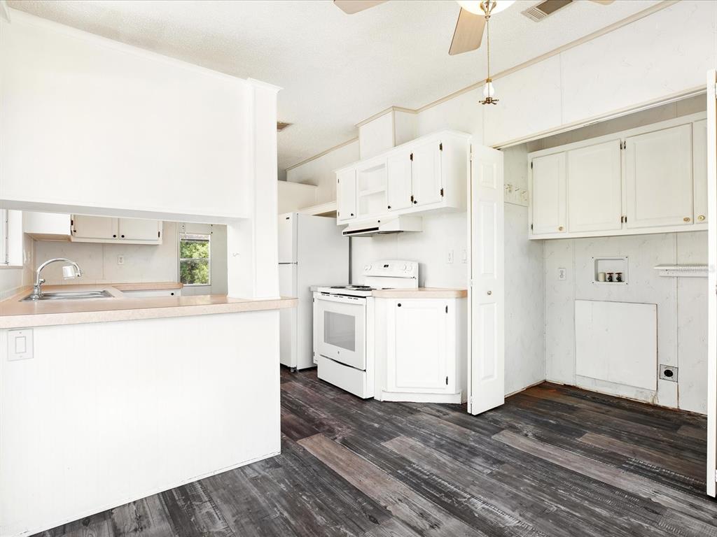 A kitchen with white cabinets, white appliances, and dark wood-look flooring — 7606 DETROIT AVENUE, HUDSON, FL