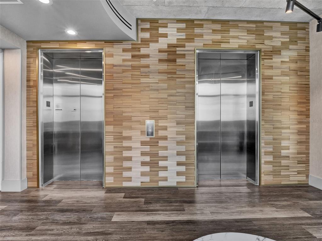 Two stainless steel elevators are set into a wall with decorative horizontal wood slat paneling — 525 E JACKSON STREET UNIT 508, ORLANDO, FL