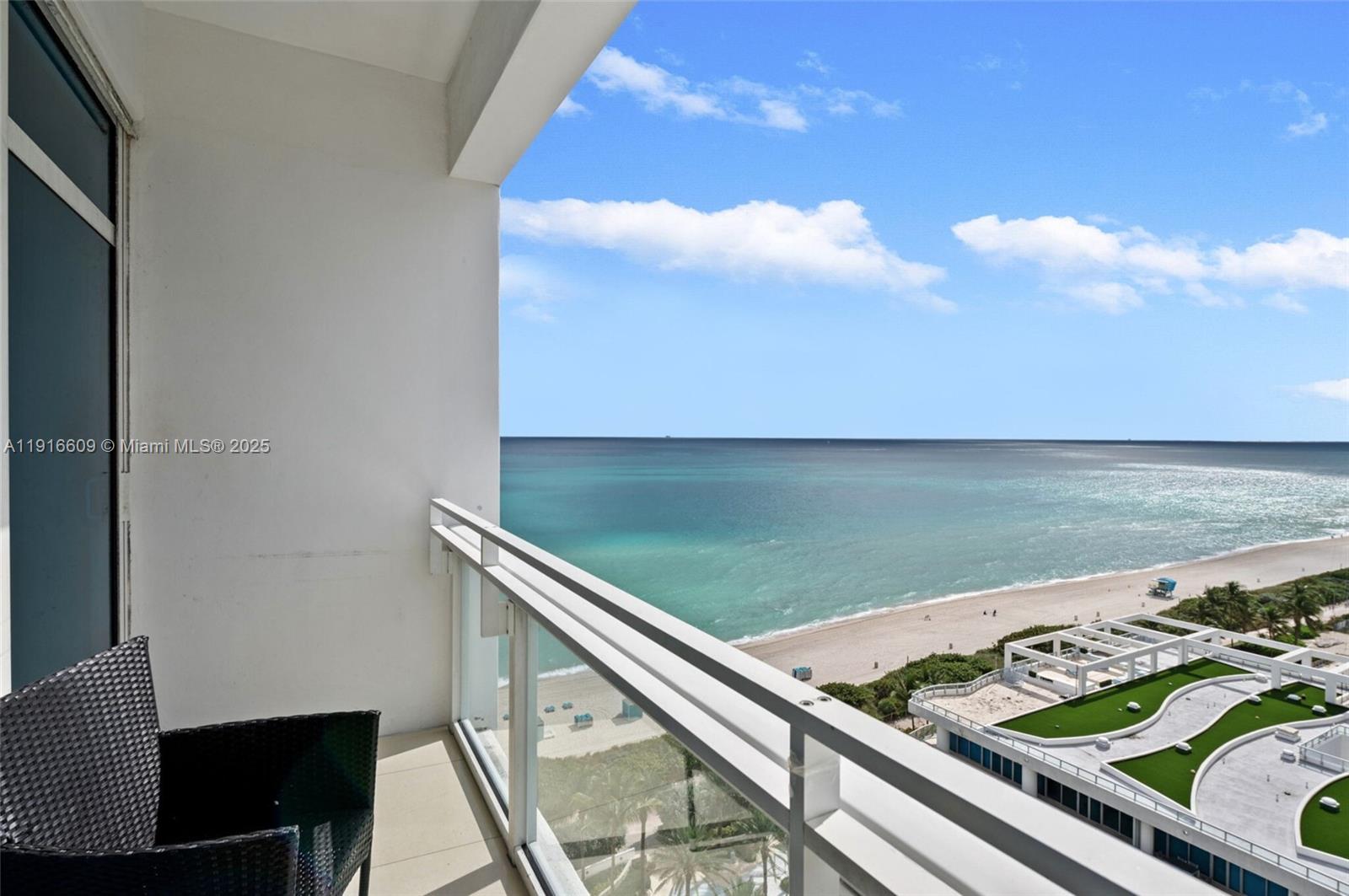 A balcony with a black chair overlooks the ocean and a nearby building rooftop — 6801 Collins Ave, Miami Beach FL 33141, MIAMI BEACH, FL