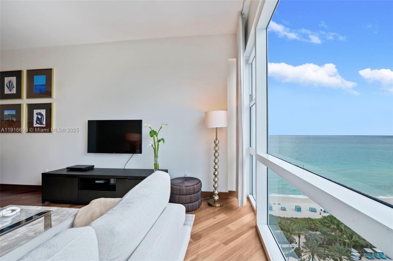A living room with a television, floor lamp, and large windows overlooking the ocean — 6801 Collins Ave, Miami Beach FL 33141, MIAMI BEACH, FL
