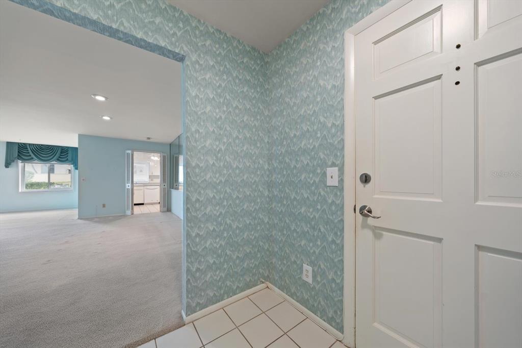 An entryway with patterned blue wallpaper, white tile flooring, and a white front door — 100 BLUFF VIEW DRIVE UNIT 114A, BELLEAIR BLUFFS, FL