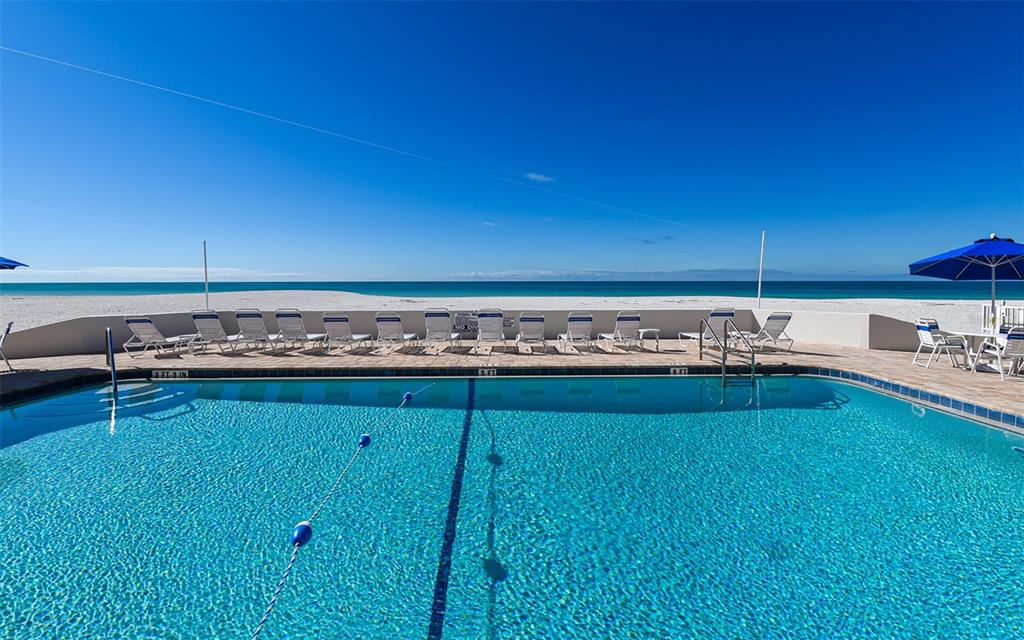 A swimming pool overlooks a sandy beach and the ocean under a clear blue sky — 1900 BENJAMIN FRANKLIN DRIVE UNIT V11, SARASOTA, FL