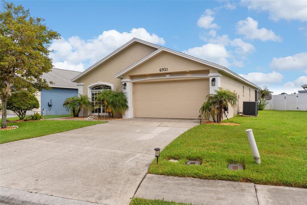 A single-story suburban house with a beige stucco exterior, a two-car garage, and a driveway — 6921 SHIMMERING DRIVE, LAKELAND, FL