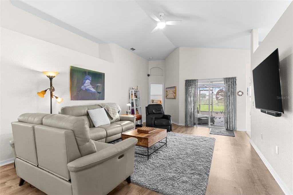 A living room features light-colored sofas, a gray area rug, and a wall-mounted television — 6921 SHIMMERING DRIVE, LAKELAND, FL