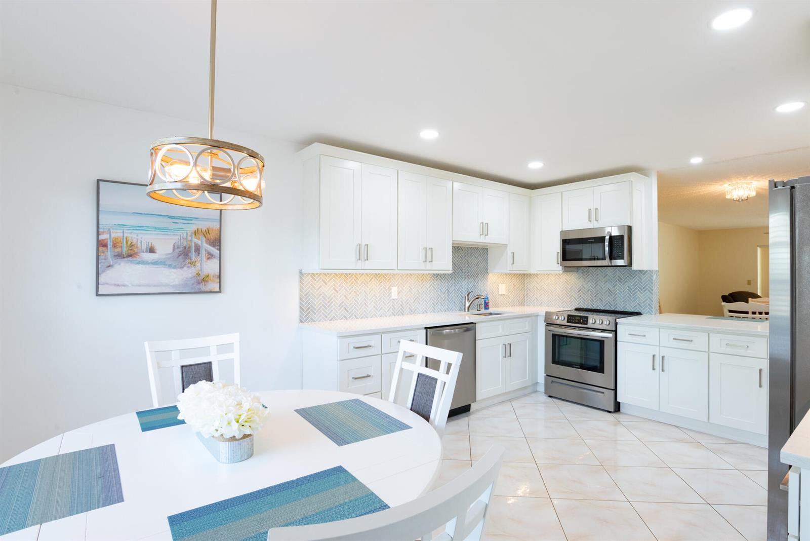 A bright kitchen features white cabinets, stainless steel appliances, and a herringbone tile backsplash — 5160 Petal Place # D, Delray Beach FL 33484, DELRAY BEACH, FL