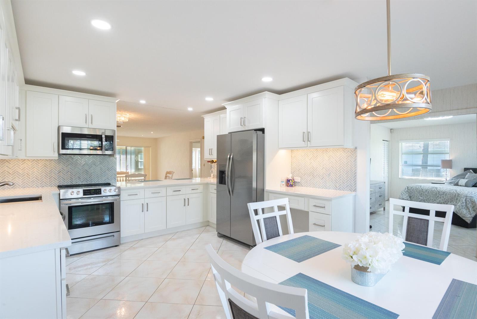 A bright kitchen features white cabinets, stainless steel appliances, and a round dining table — 5160 Petal Place # D, Delray Beach FL 33484, DELRAY BEACH, FL