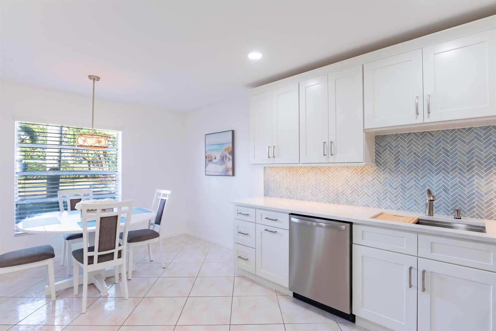 A kitchen with white cabinets, a herringbone backsplash, and an adjacent dining area — 5160 Petal Place # D, Delray Beach FL 33484, DELRAY BEACH, FL