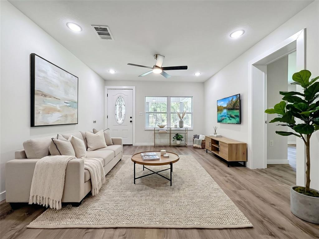 A living room features a beige sofa, round coffee table, wall-mounted television, and light flooring — 317 NE 13TH TERRACE, CRYSTAL RIVER, FL