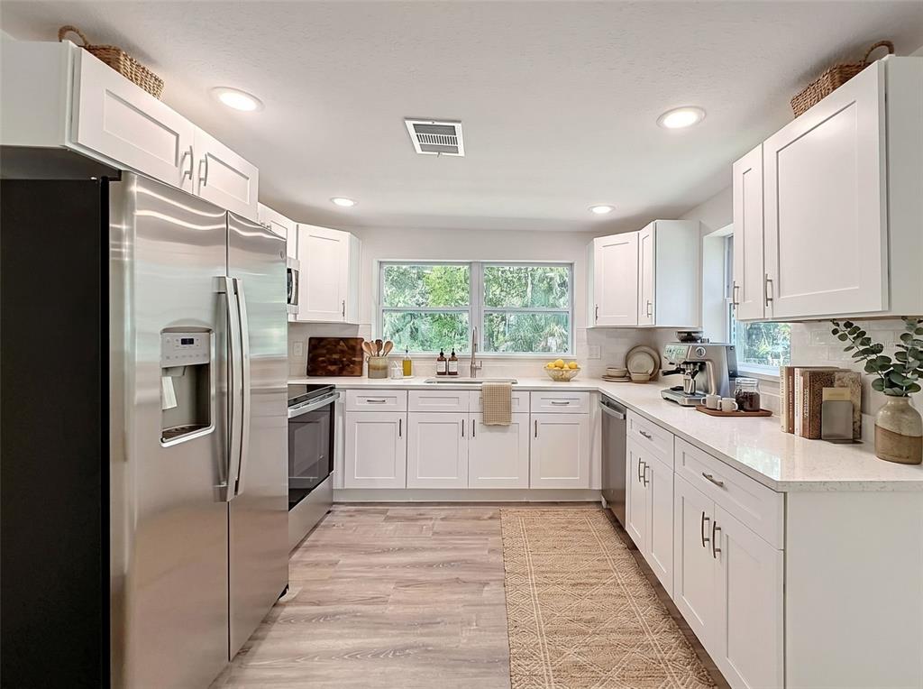 A bright kitchen features white cabinets, stainless steel appliances, and light wood-look flooring — 317 NE 13TH TERRACE, CRYSTAL RIVER, FL