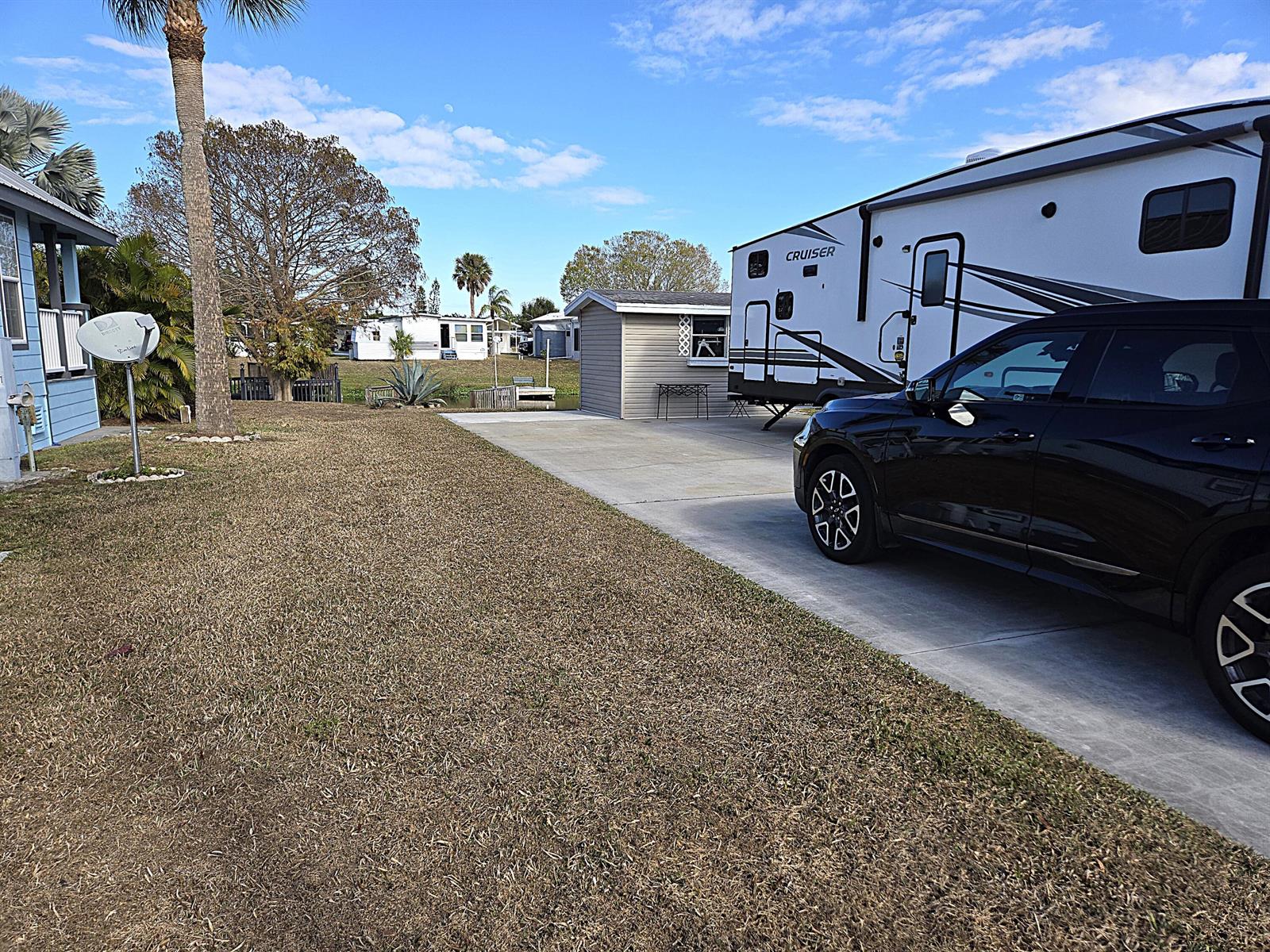 A black SUV is parked on a concrete driveway next to a travel trailer — 14031 SE 126th Terrace, Okeechobee FL 34974, OKEECHOBEE, FL