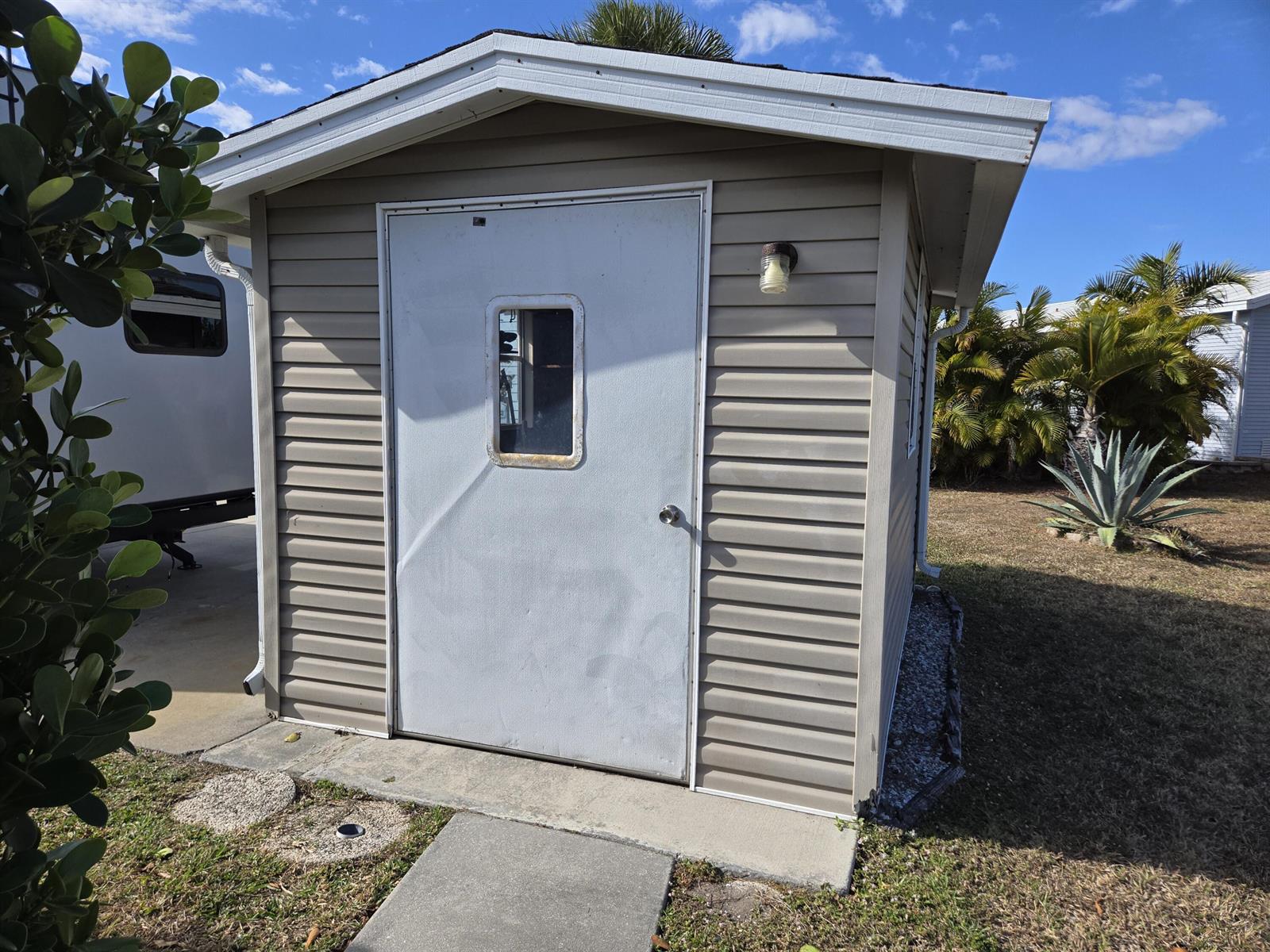 A beige vinyl-sided shed with a white door and a small window stands outdoors — 14031 SE 126th Terrace, Okeechobee FL 34974, OKEECHOBEE, FL